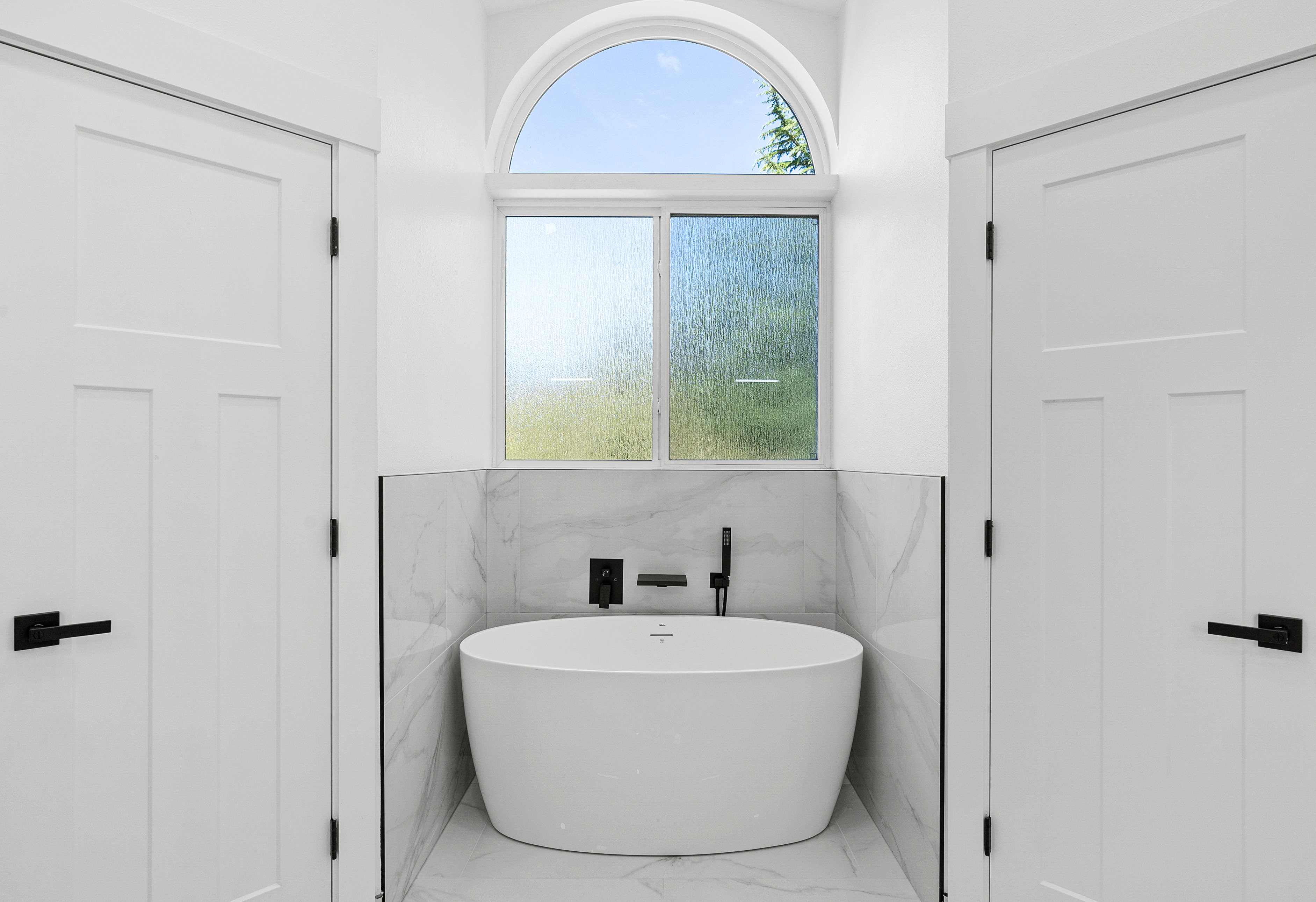 Remodeled bathroom with freestanding tub beneath an arched window